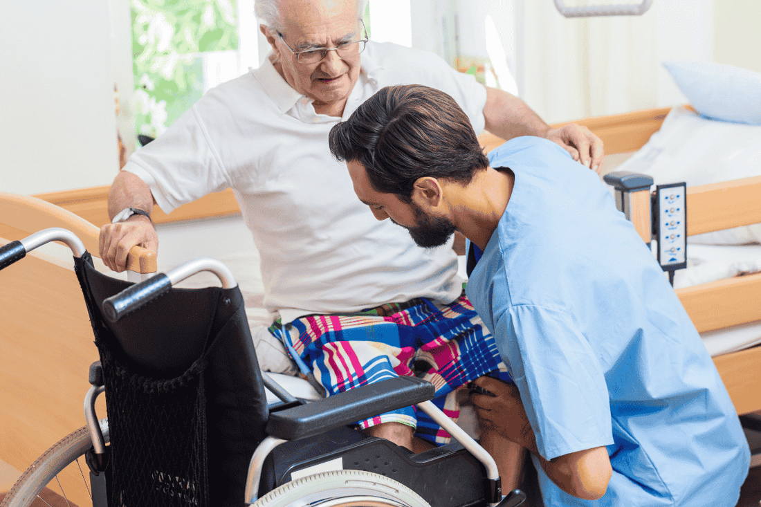older man being helped into wheelchair by a carer 