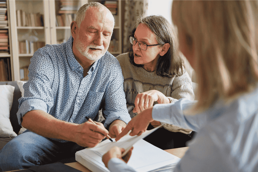 An older man signing a legal document with his partner and lawyer present 