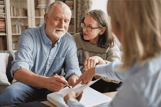 An older man signing a legal document with his partner and lawyer present 