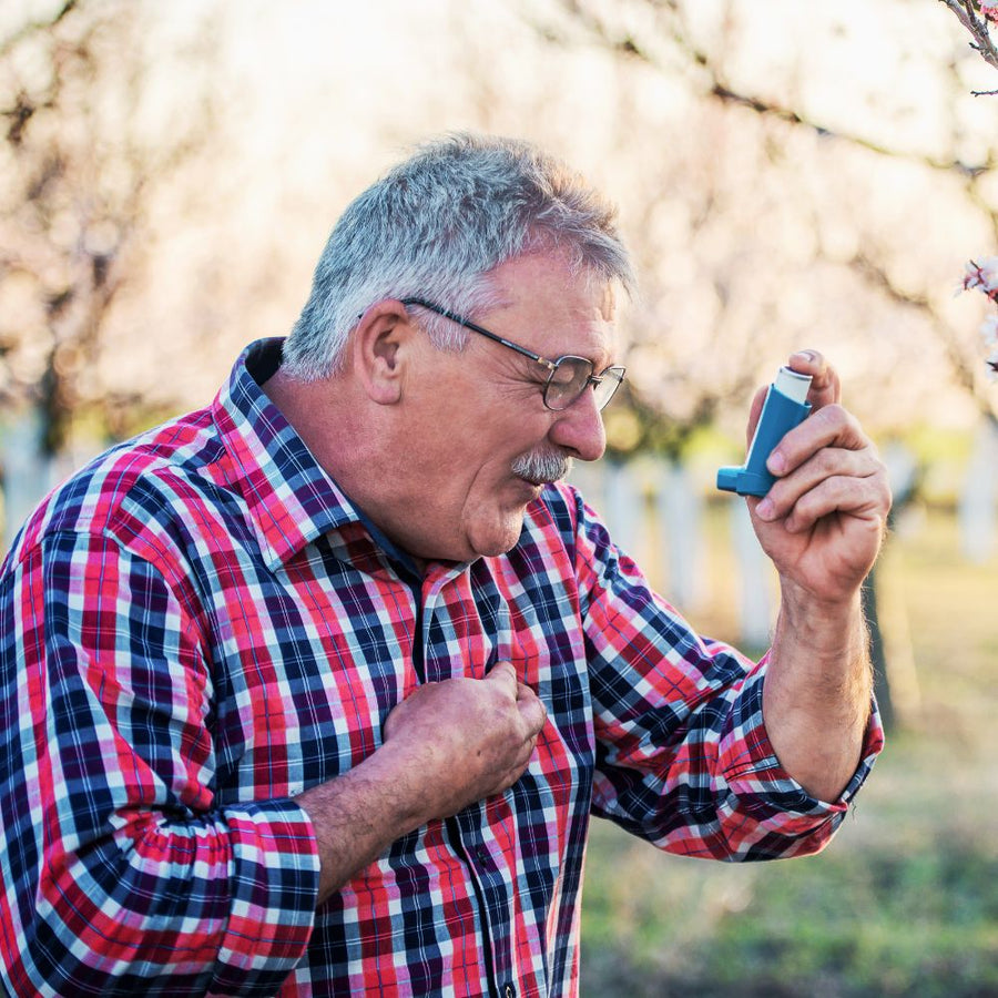 Man in a plaid shirt using an asthma inhaler outdoors.