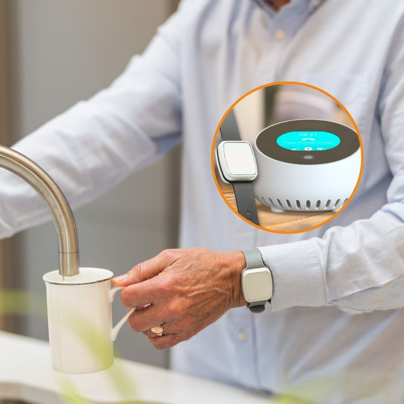 Elderly man filling a mug in the kitchen while wearing a digital fall detection wristband. Inset shows the HelpAlert digital lifeline alarm base unit on a table, providing 24/7 monitoring and emergency connection at home.