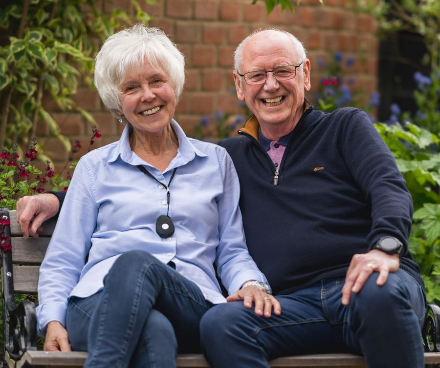 Older couple wearing a personal alarm pendant while relaxing in their garden for safety and peace of mind