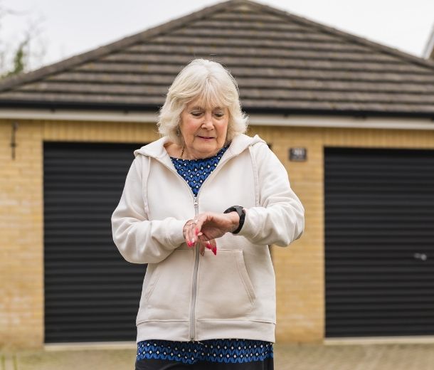 Elderly woman wearing a HelpAlert fall prevention watch, checking the device while walking outdoors.