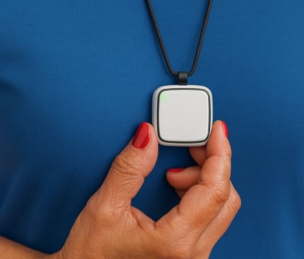 HelpAlert lifeline personal alarm on a neck lanyard, held against a blue top with red-polished nails, SOS ready