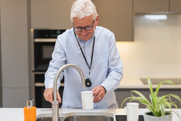 Older man wearing a HelpAlert personal alarm pendant while making a drink in the kitchen