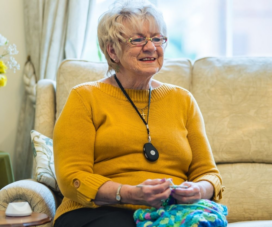 Woman sitting on a couch wearing a yellow sweater and glasses, holding a colorful object.