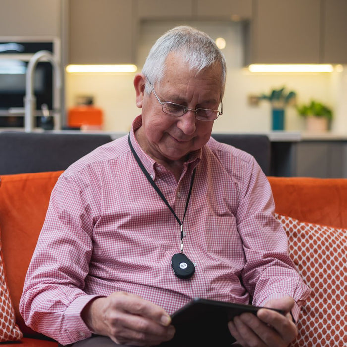 Elderly man sitting on a sofa wearing a HelpAlert fall detection pendant alarm around his neck