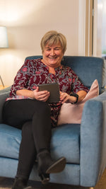 Woman sitting on a blue couch holding a tablet, smiling.
