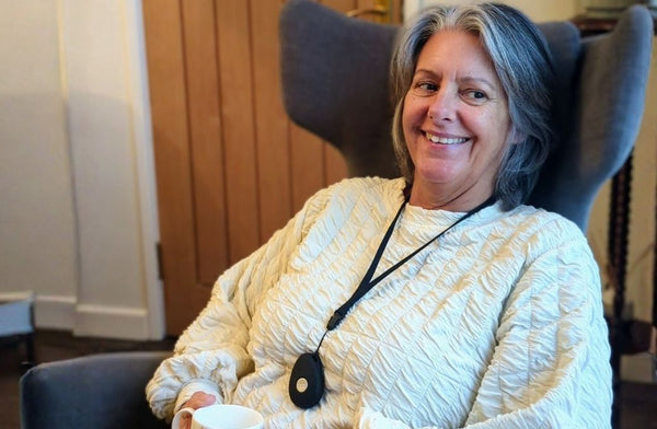 Older woman sitting comfortably at home wearing a personal alarm pendant