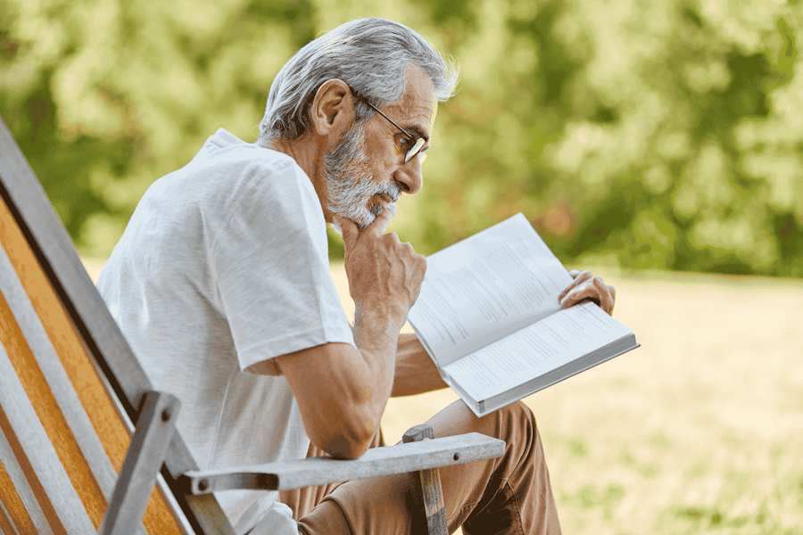 older man reading a book outdoors 