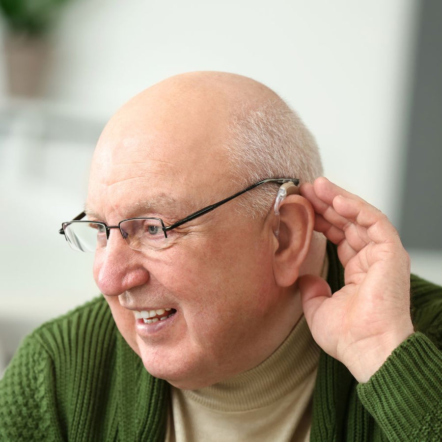 Man adjusting a hearing aid with a blurred indoor background