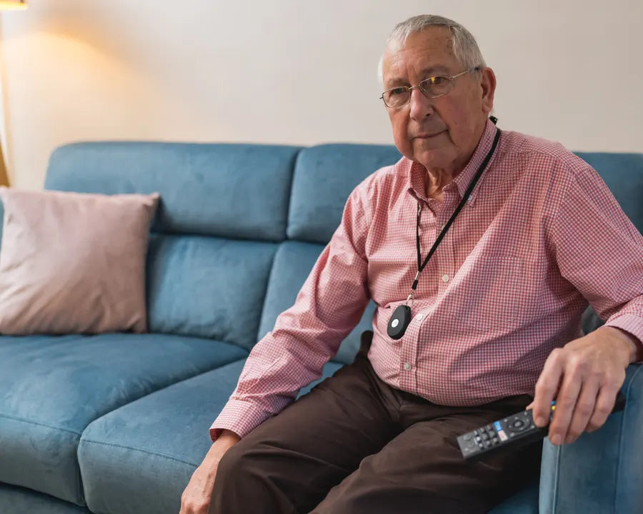 An older man relaxing on his sofa wearing a HelpAlert Fall Pendant on a lanyard